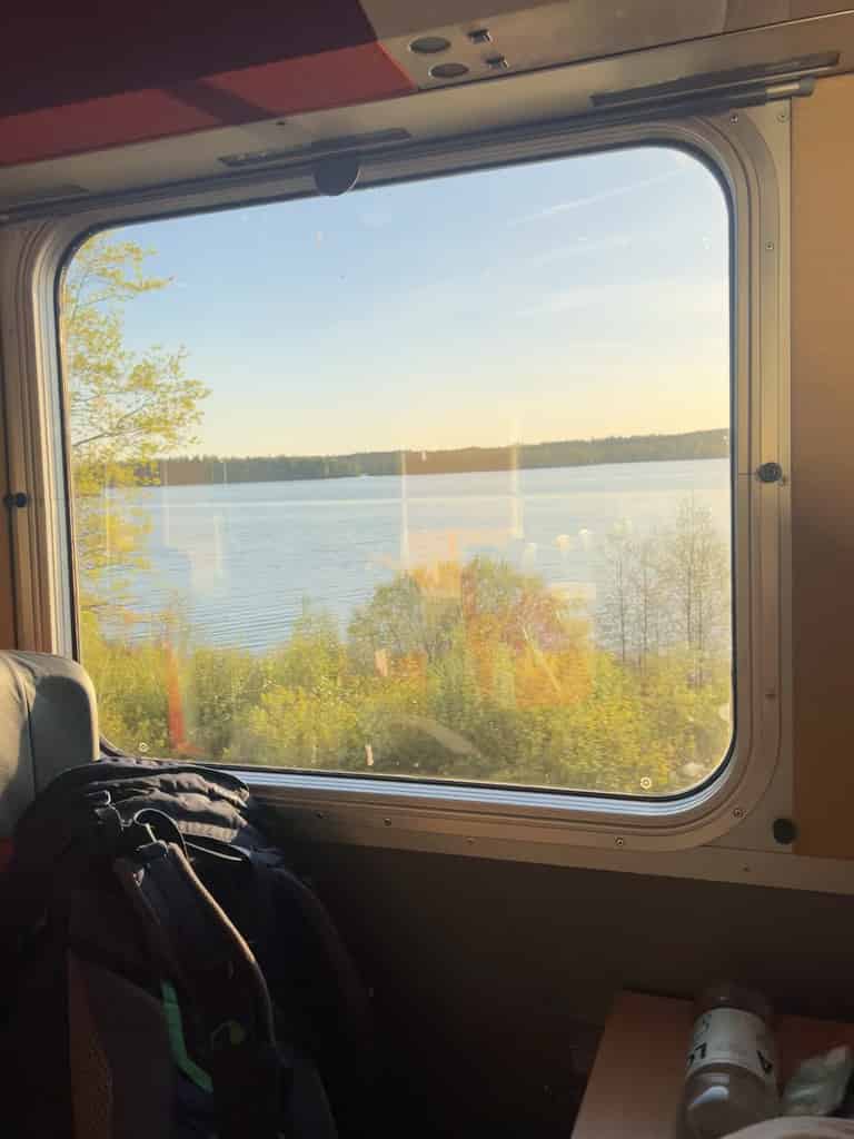 Ein Blick aus dem Fenster eines Zuges auf einen See und Wald bei Sonnenuntergang.
